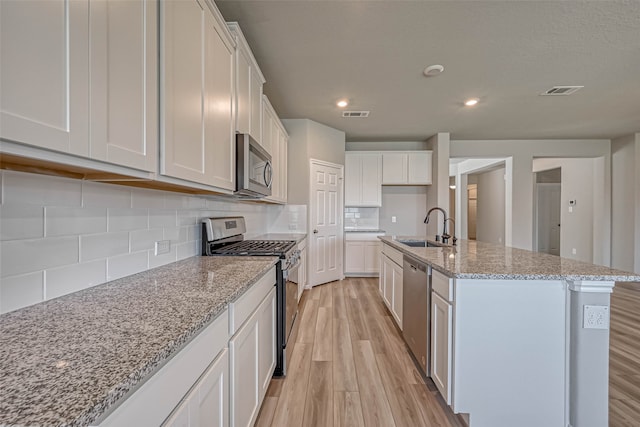 kitchen featuring stainless steel appliances, sink, light hardwood / wood-style flooring, white cabinetry, and an island with sink