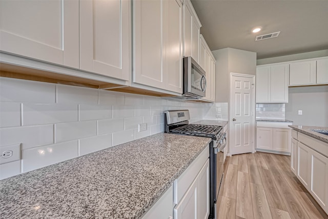 kitchen with light stone countertops, backsplash, stainless steel appliances, light hardwood / wood-style flooring, and white cabinets