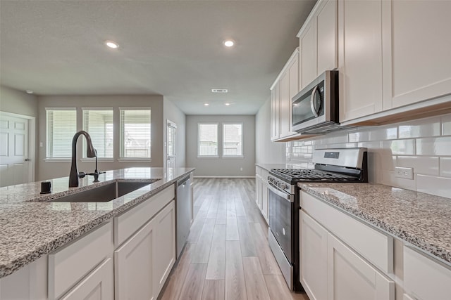 kitchen featuring sink, light hardwood / wood-style floors, light stone counters, white cabinetry, and stainless steel appliances