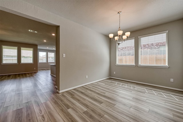 spare room featuring a notable chandelier and light wood-type flooring