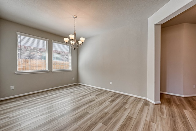 empty room featuring a textured ceiling, light wood-type flooring, and a notable chandelier