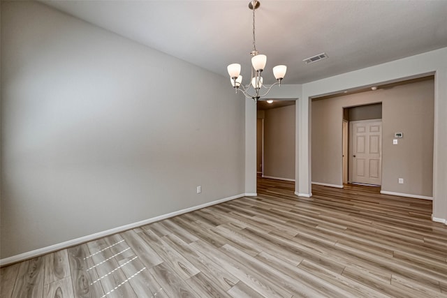 unfurnished room featuring an inviting chandelier and light hardwood / wood-style flooring