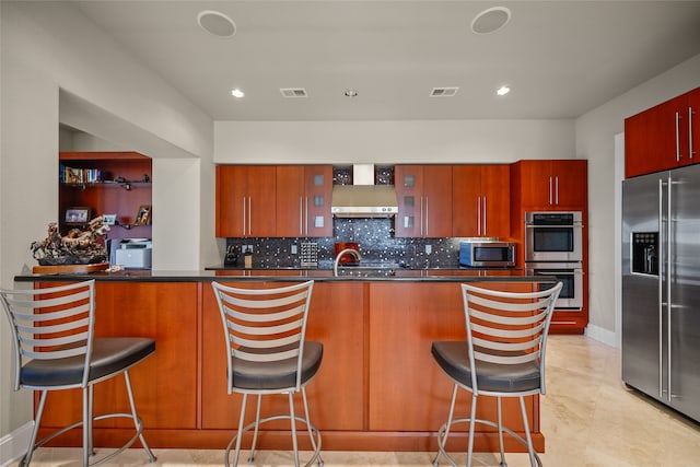 kitchen featuring a kitchen bar, appliances with stainless steel finishes, decorative backsplash, and kitchen peninsula