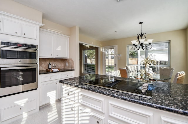 kitchen with black electric stovetop, stainless steel double oven, white cabinetry, and an inviting chandelier