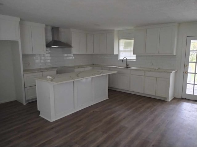 kitchen featuring white cabinets, a healthy amount of sunlight, a kitchen island, and wall chimney range hood