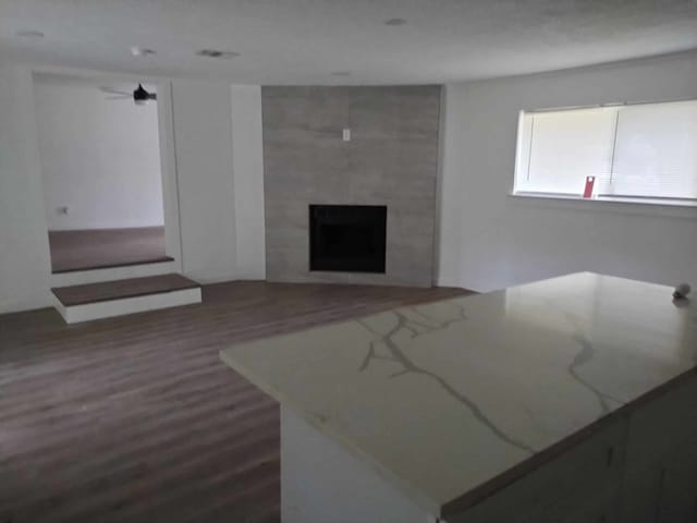 unfurnished living room with ceiling fan, a fireplace, and dark wood-type flooring