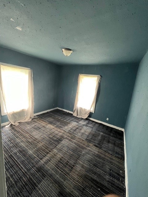 spare room featuring dark carpet and a textured ceiling