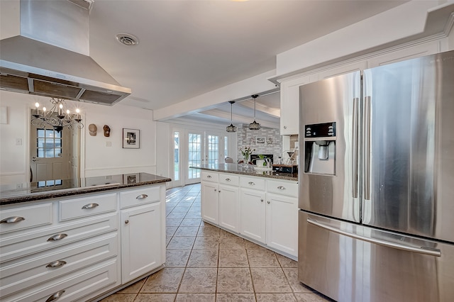 kitchen with white cabinetry, hanging light fixtures, stainless steel fridge, dark stone counters, and island range hood