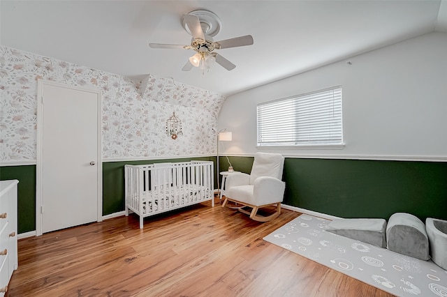 bedroom with a crib, hardwood / wood-style flooring, vaulted ceiling, and ceiling fan