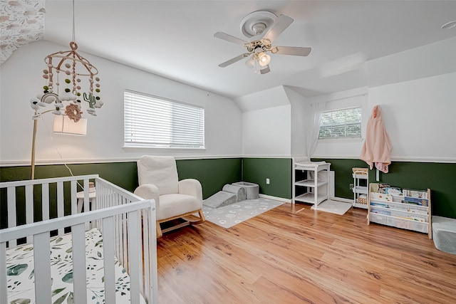 bedroom with ceiling fan, hardwood / wood-style floors, a nursery area, and lofted ceiling