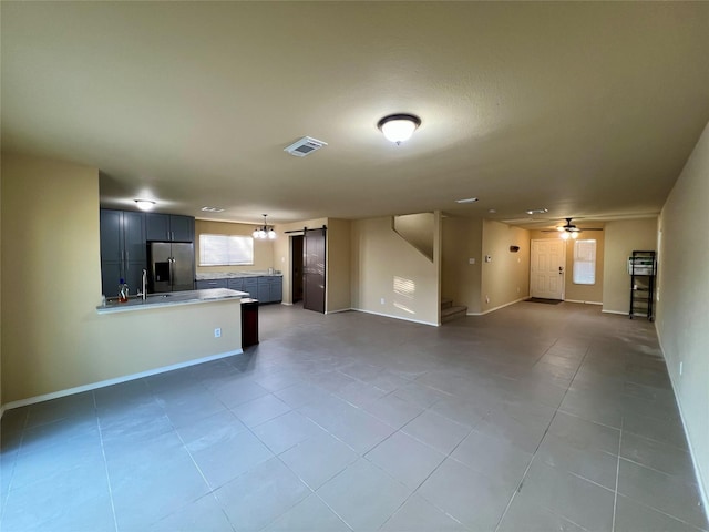 unfurnished living room featuring a barn door, ceiling fan, and tile patterned flooring