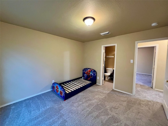 unfurnished bedroom with a textured ceiling, carpet floors, and ensuite bath