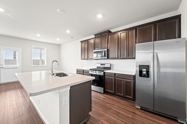 kitchen with dark wood-type flooring, sink, decorative backsplash, an island with sink, and appliances with stainless steel finishes