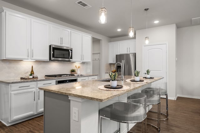 kitchen with dark hardwood / wood-style floors, an island with sink, decorative light fixtures, white cabinetry, and stainless steel appliances