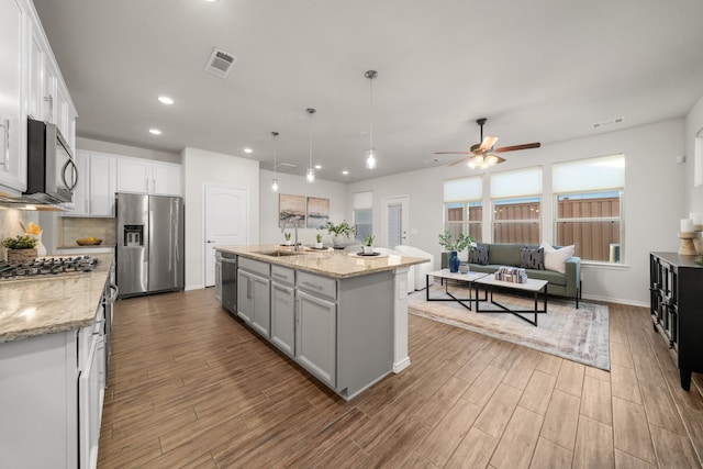 kitchen with stainless steel appliances, sink, decorative light fixtures, white cabinetry, and an island with sink