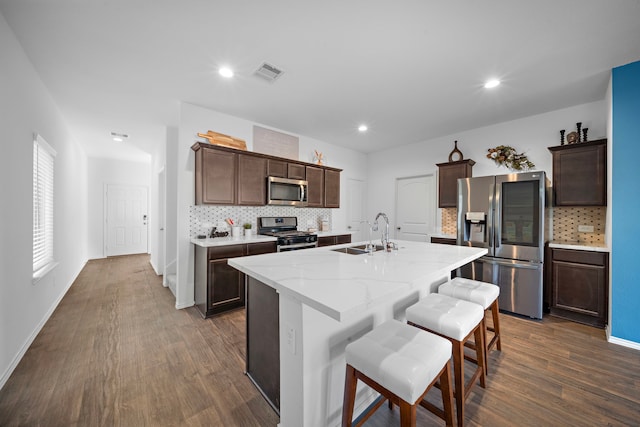 kitchen with appliances with stainless steel finishes, dark hardwood / wood-style flooring, backsplash, sink, and an island with sink