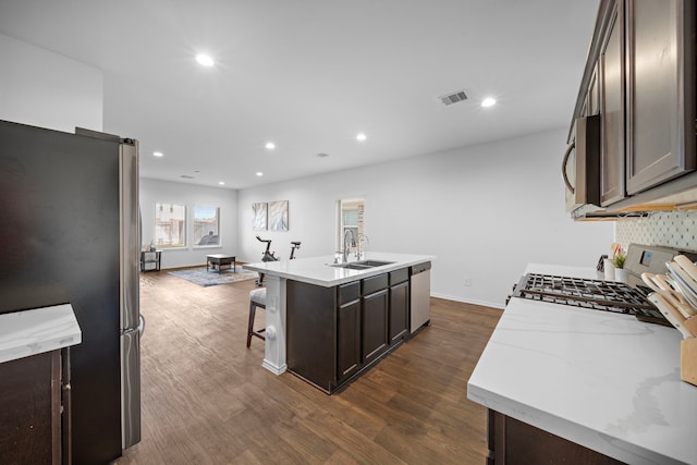 kitchen with appliances with stainless steel finishes, dark brown cabinets, dark wood-type flooring, sink, and an island with sink