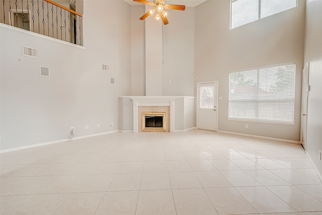 unfurnished living room with ceiling fan, light tile patterned floors, a towering ceiling, and a tile fireplace