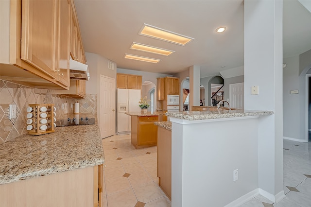 kitchen with a center island, light stone countertops, white appliances, and kitchen peninsula