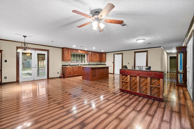 kitchen featuring pendant lighting, crown molding, a textured ceiling, a kitchen island, and wood-type flooring