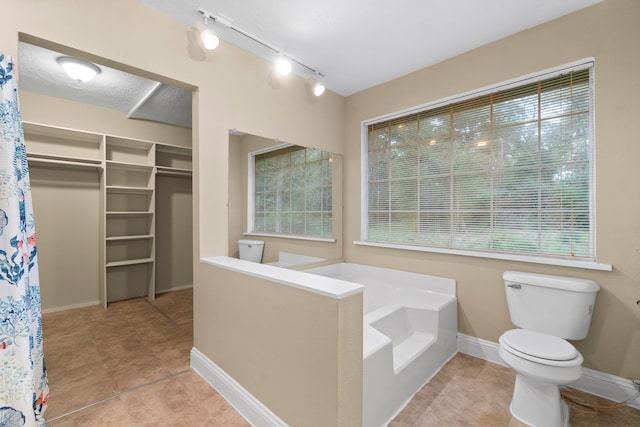 bathroom with a tub to relax in, tile patterned flooring, track lighting, and toilet