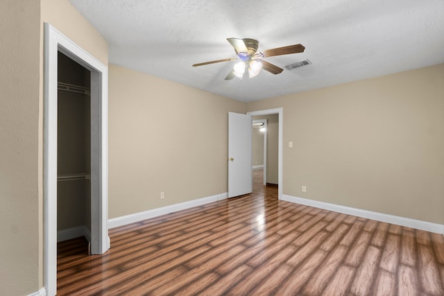 unfurnished bedroom with a walk in closet, a textured ceiling, ceiling fan, wood-type flooring, and a closet