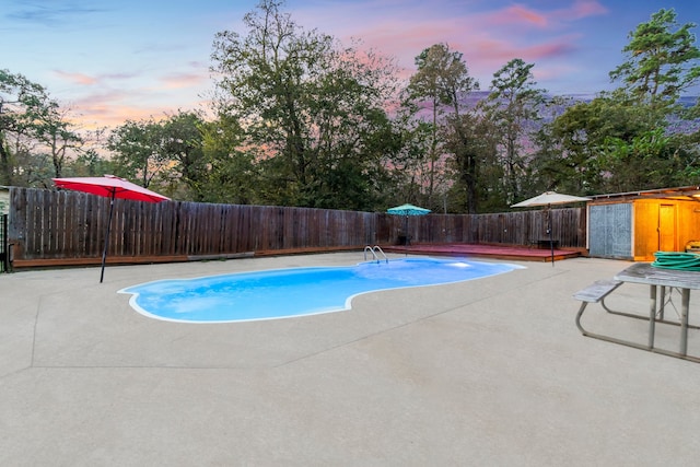 pool at dusk featuring a storage unit and a patio