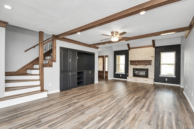 unfurnished living room featuring a textured ceiling, ceiling fan, lofted ceiling with beams, hardwood / wood-style flooring, and a fireplace