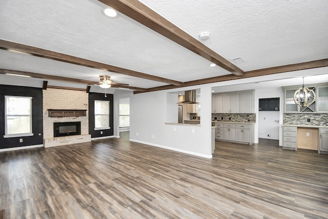 unfurnished living room with dark hardwood / wood-style flooring, a fireplace, beamed ceiling, and a textured ceiling