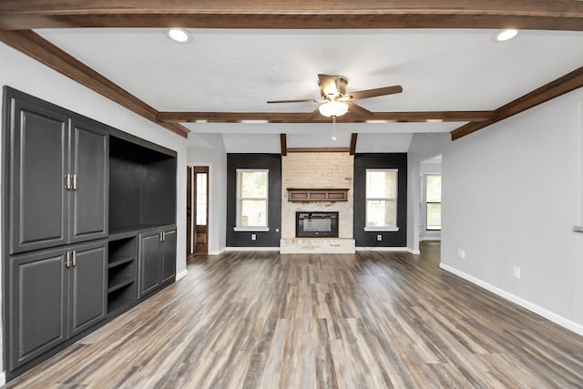 unfurnished living room with beamed ceiling, dark hardwood / wood-style flooring, a wealth of natural light, and a fireplace