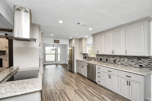 kitchen with hardwood / wood-style floors, wall chimney exhaust hood, a fireplace, appliances with stainless steel finishes, and light stone counters