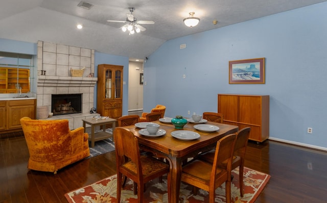 dining room featuring a textured ceiling, dark wood-type flooring, vaulted ceiling, ceiling fan, and a tiled fireplace