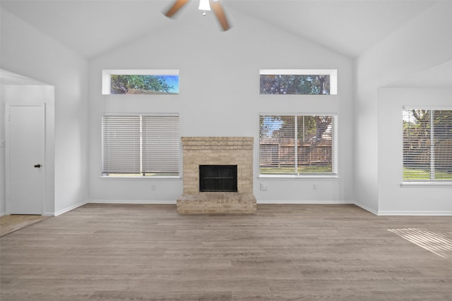 unfurnished living room with ceiling fan, light wood-type flooring, high vaulted ceiling, and a brick fireplace