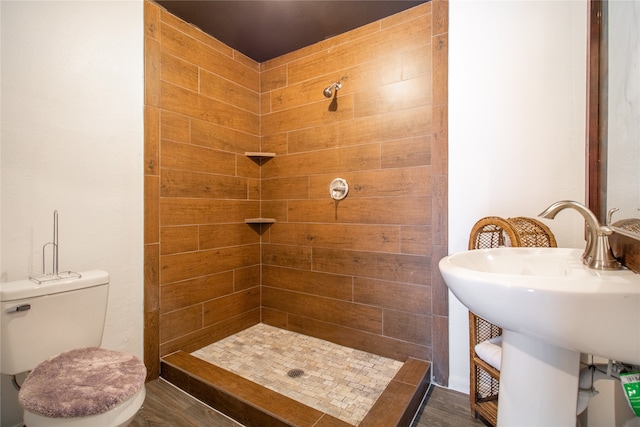 bathroom with toilet, sink, wood-type flooring, and tiled shower