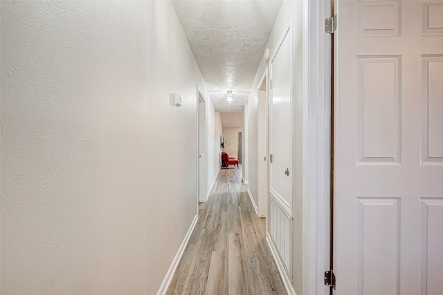 corridor featuring a textured ceiling and light hardwood / wood-style flooring