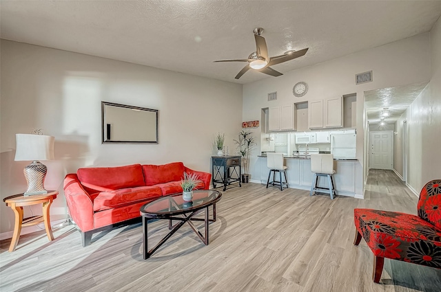 living room featuring ceiling fan, a textured ceiling, and light wood-type flooring