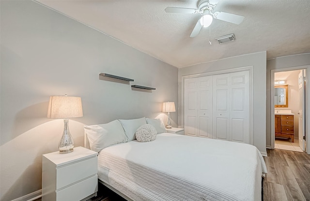 bedroom featuring ensuite bath, a textured ceiling, light wood-type flooring, a closet, and ceiling fan