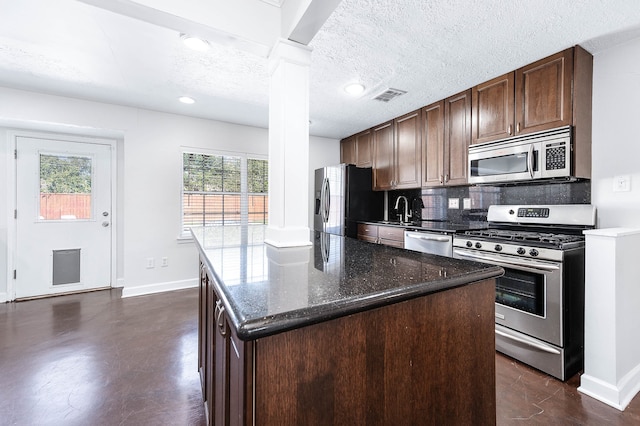 kitchen with stainless steel appliances, dark stone countertops, a textured ceiling, decorative backsplash, and a kitchen island