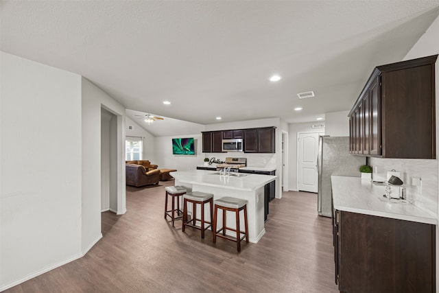 kitchen featuring appliances with stainless steel finishes, dark hardwood / wood-style flooring, a breakfast bar, dark brown cabinets, and a kitchen island