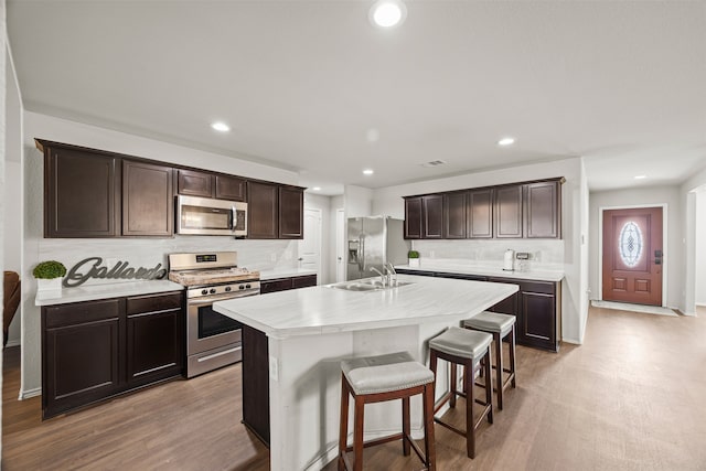 kitchen featuring appliances with stainless steel finishes, light wood-type flooring, a kitchen island with sink, sink, and a breakfast bar area