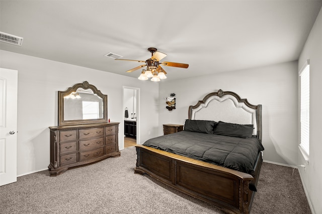 bedroom featuring ceiling fan, light colored carpet, multiple windows, and ensuite bath