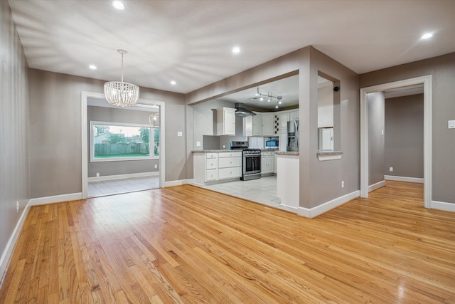 kitchen with white cabinets, stainless steel appliances, decorative light fixtures, and light wood-type flooring