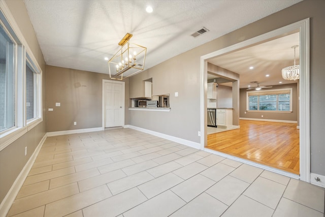 unfurnished living room featuring ceiling fan with notable chandelier, a textured ceiling, and light hardwood / wood-style flooring