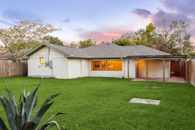 back house at dusk with a patio area and a yard