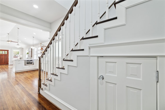 staircase with ceiling fan, wood-type flooring, and lofted ceiling