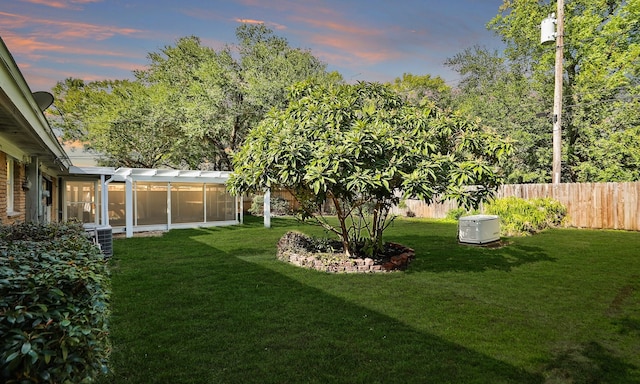 yard at dusk with central AC unit and a sunroom