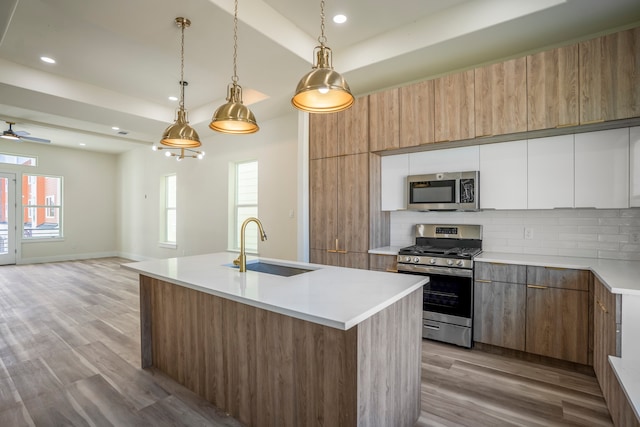 kitchen featuring appliances with stainless steel finishes, sink, decorative light fixtures, light hardwood / wood-style flooring, and white cabinetry