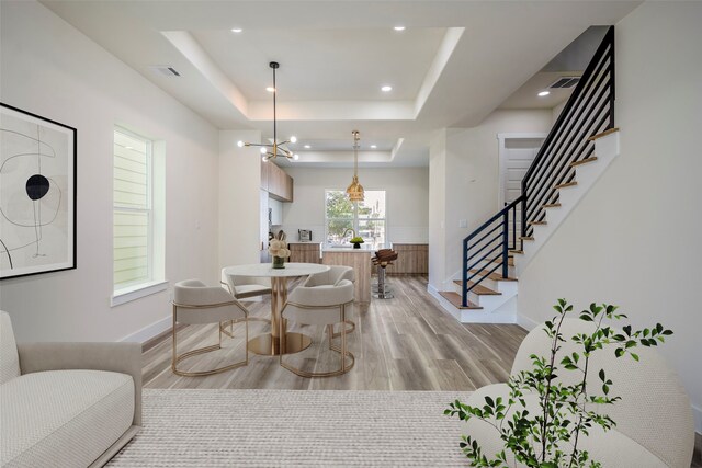 dining space with a chandelier, light wood-type flooring, and a raised ceiling