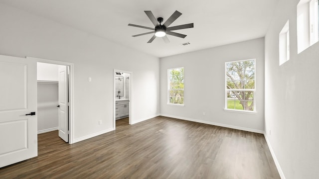 unfurnished bedroom with ensuite bath, ceiling fan, dark wood-type flooring, a walk in closet, and a closet