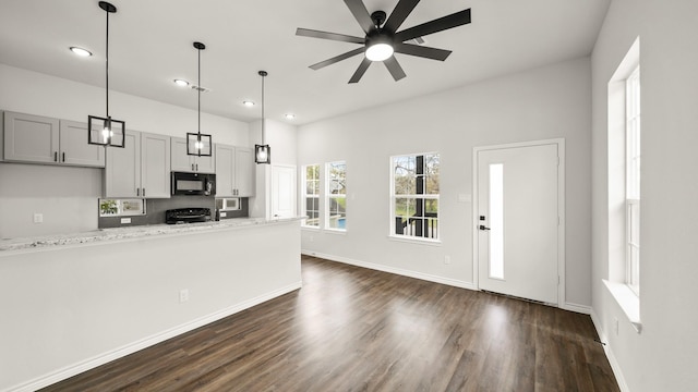 kitchen with light stone countertops, ceiling fan, dark hardwood / wood-style floors, pendant lighting, and black appliances